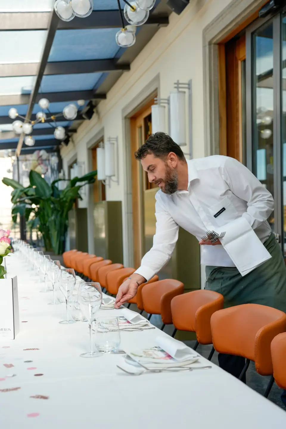 Eine lange, festlich gedeckte Tafel mit orangen Lederstühlen wird vorbereitet