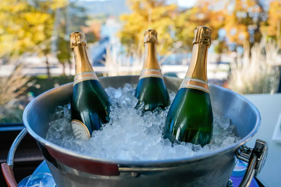 Drei Champagnerflaschen in einem Eiskübel, dahinter Herbstbäume
