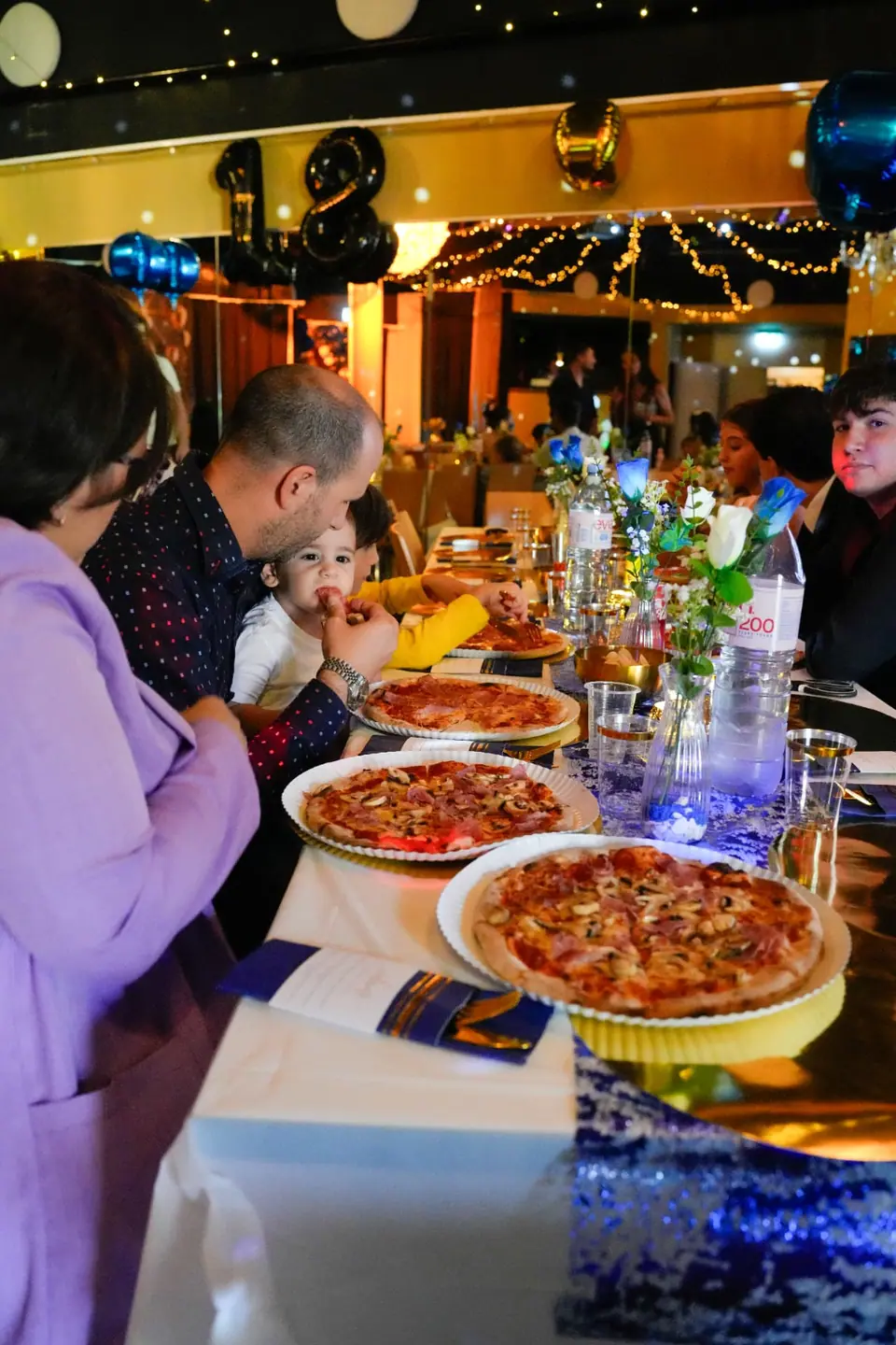 Familie und Freunde geniessen gemeinsam Pizza an der Geburtstagstafel