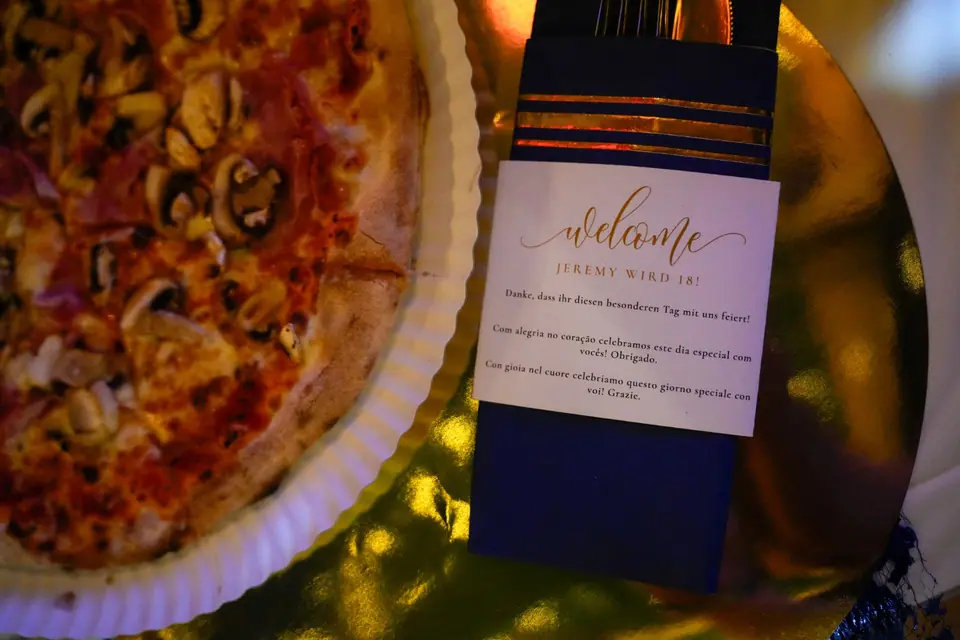 Willkommenskarte neben Pizza am festlich gedeckten Platz