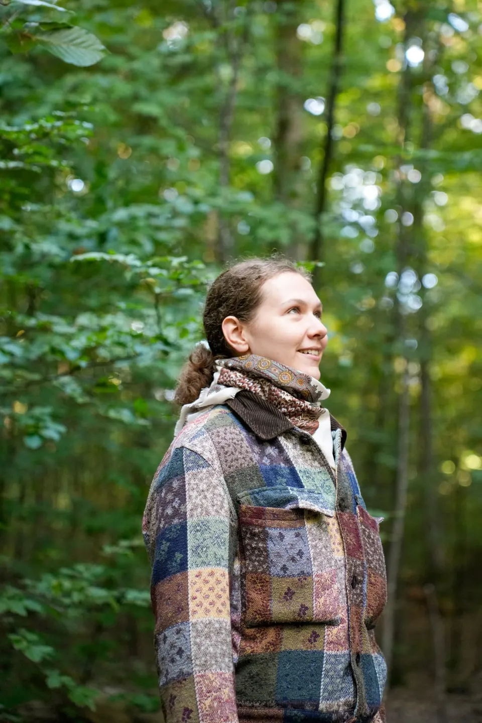 Teilnehmerin blickt lächelnd ins Blätterdach während des Forest Bathing