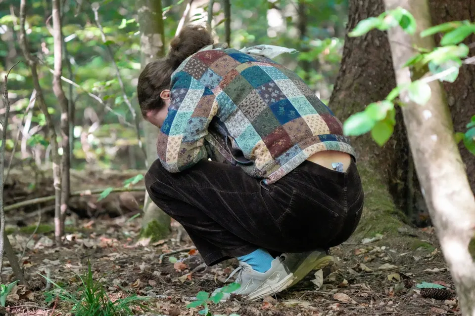 Teilnehmerin hockt achtsam am Waldboden und betrachtet Naturdetails